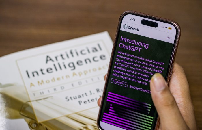 Close-up of a smartphone displaying ChatGPT app held over AI textbook.