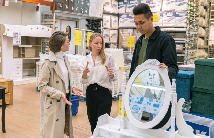 Three adults discussing a vanity set in a furniture store, engaging in shopping decisions.