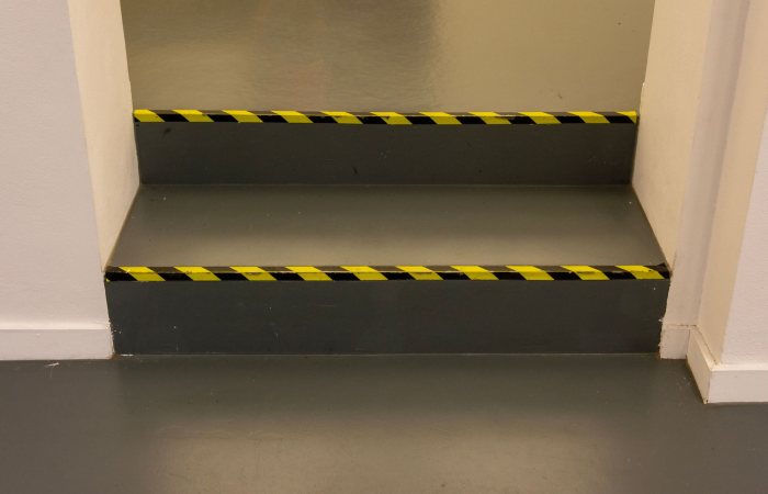 Green steps with black and yellow caution tape in an interior hallway for safety.