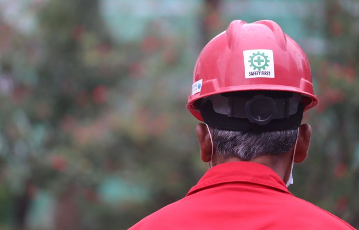 A worker focusing on safety outdoors, wearing a red helmet with a safety logo.