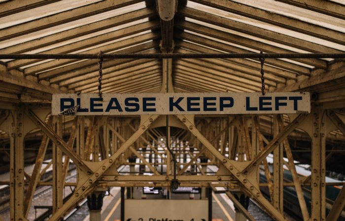 Vintage metal construction on railway station with platform under old roof and sign saying Please keep left