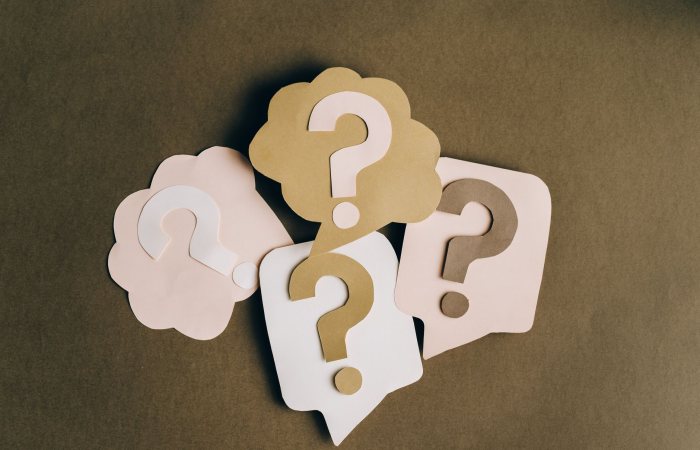 Four paper cutouts of question marks in beige and white on a brown surface, symbolizing inquiry and curiosity.